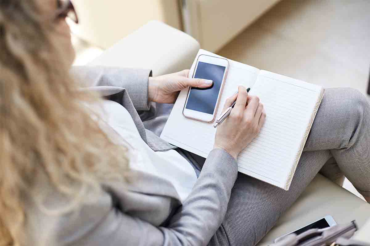 phone, fintech notebook, and coffee cup on table, with a hand over the notebook with a pen.