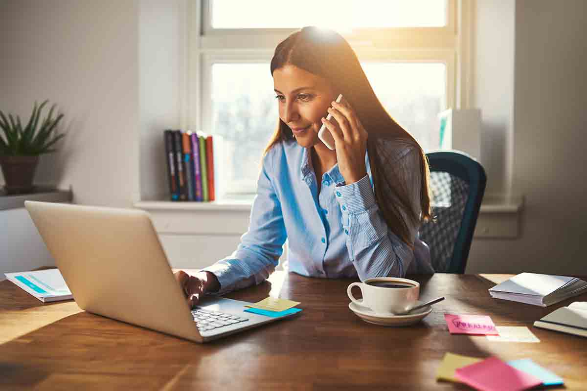phone, fintech notebook, and coffee cup on table, with a hand over the notebook with a pen.